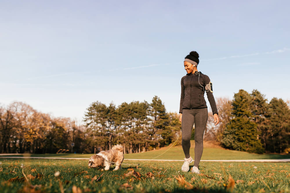 Mulher negra caminhando com seu cachorro no parque.
